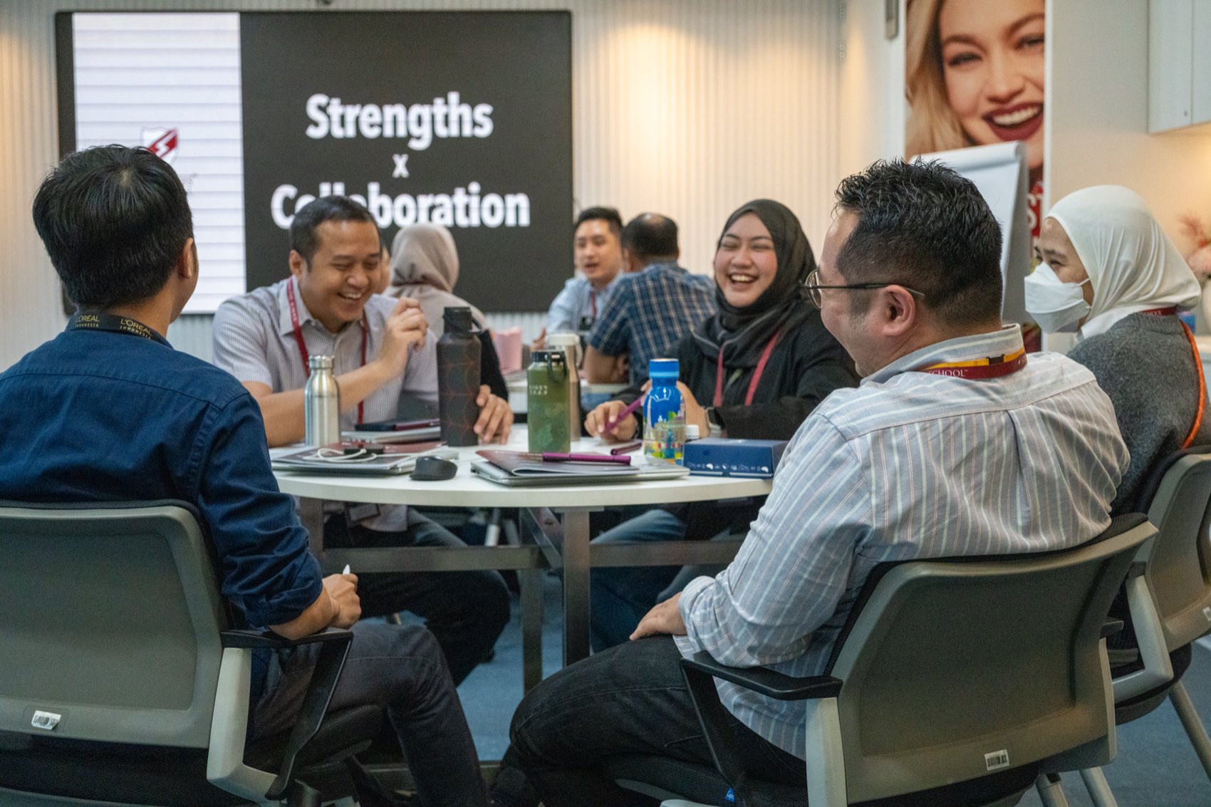 Colleagues around a table mid-conversation, with “Strengths × Collaboration” on the board behind them.