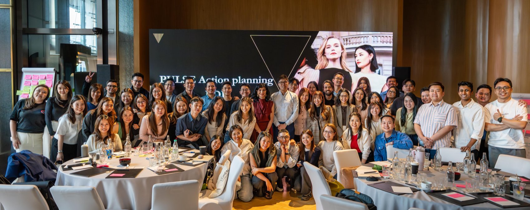 A luxury retail cohort gathered at the end of an action-planning day, in front of the room’s screen.